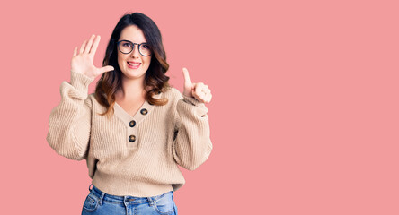 Beautiful young brunette woman wearing casual clothes and glasses showing and pointing up with fingers number six while smiling confident and happy.