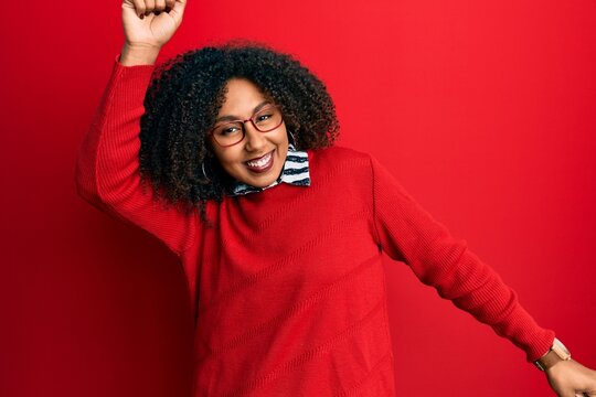 Beautiful african american woman with afro hair wearing sweater and glasses dancing happy and cheerful, smiling moving casual and confident listening to music
