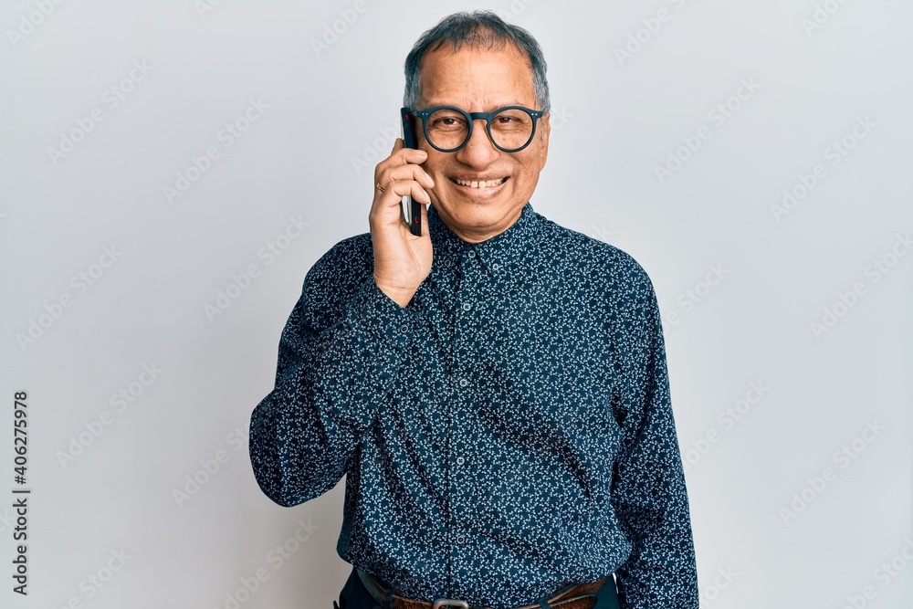 Poster middle age indian man having conversation talking on the smartphone looking positive and happy stand