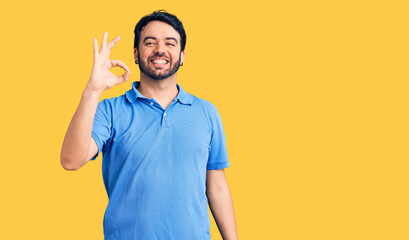 Young hispanic man wearing casual clothes smiling positive doing ok sign with hand and fingers. successful expression.