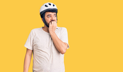 Young hispanic man wearing bike helmet looking stressed and nervous with hands on mouth biting nails. anxiety problem.
