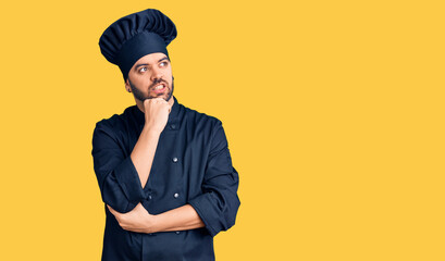 Young hispanic man wearing cooker uniform with hand on chin thinking about question, pensive expression. smiling with thoughtful face. doubt concept.