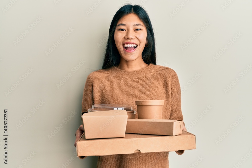 Wall mural young chinese woman holding take away food smiling and laughing hard out loud because funny crazy jo