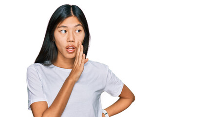 Beautiful young asian woman wearing casual white t shirt hand on mouth telling secret rumor, whispering malicious talk conversation