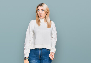 Young caucasian woman wearing casual winter sweater in shock face, looking skeptical and sarcastic, surprised with open mouth