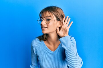 Teenager caucasian girl wearing casual clothes and glasses smiling with hand over ear listening and hearing to rumor or gossip. deafness concept.