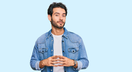 Young hispanic man wearing casual clothes hands together and fingers crossed smiling relaxed and cheerful. success and optimistic