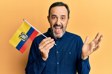 Middle age hispanic man holding ecuador flag celebrating achievement with happy smile and winner expression with raised hand - obrazy, fototapety, plakaty