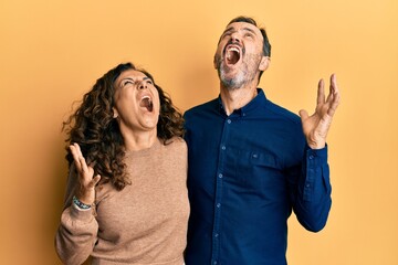 Middle age hispanic couple wearing casual clothes crazy and mad shouting and yelling with aggressive expression and arms raised. frustration concept.