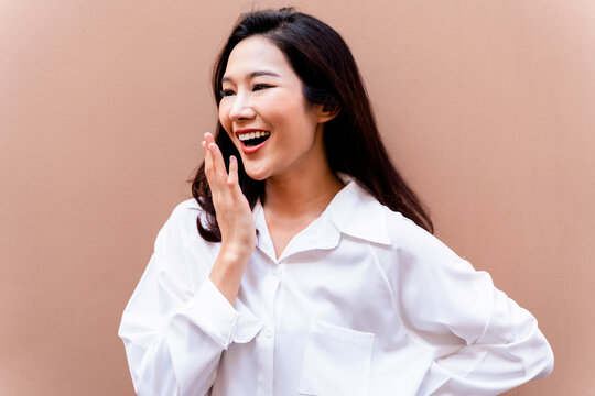 20s Young Asian Happy Millenial Woman In White Shirt In Clean Background Smiling And Laughing Confidently With Beautiful Teeth. Portrait Of Beauty Skin Care And Oral Care Concept