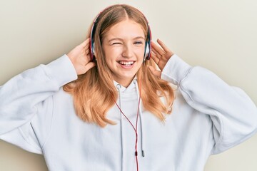 Beautiful young caucasian girl listening to music using headphones winking looking at the camera...