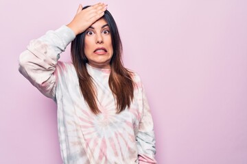 Young beautiful brunette woman wearing casual dyed sweatshirt over isolated pink background surprised with hand on head for mistake, remember error. Forgot, bad memory concept.