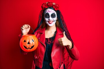 Woman wearing day of the dead costume holding pumpkin smiling happy and positive, thumb up doing excellent and approval sign