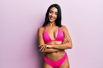 Beautiful hispanic woman wearing bikini happy face smiling with crossed arms looking at the camera....