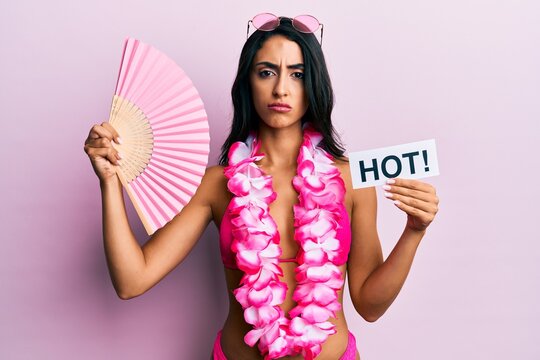Beautiful hispanic woman wearing bikini and handfan holding hot word skeptic and nervous, frowning upset because of problem. negative person.