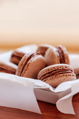 Chocolate macarons served on parchment paper and white plate on wood surface
