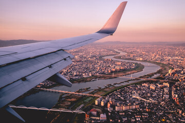 Plane wing and beautiful sunset over Osaka cityscape, Japan
