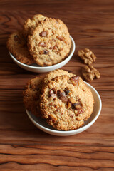Oatmeal cookies with walnuts and raisins on small saucers standing on a wooden table. Closeup