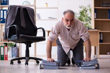 Fototapeta na wymiar Old male employee doing physical exercises at workplace
