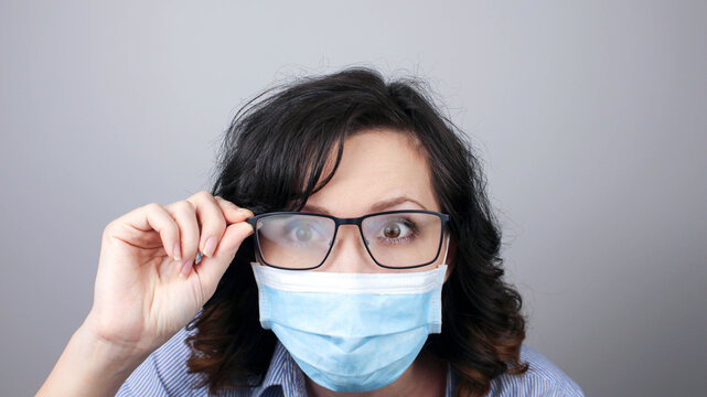 Young woman with foggy glasses caused by wearing disposable mask on white background. Protective measure during coronavirus pandemic