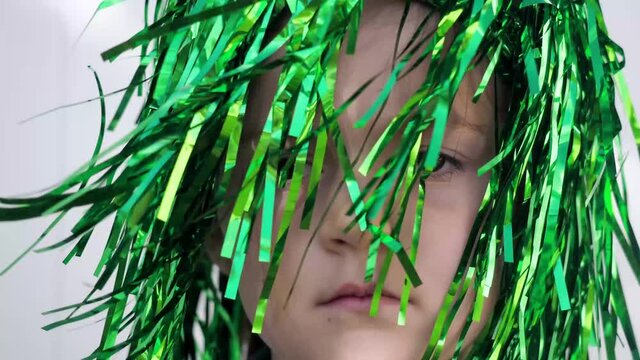 Sad girl with brown eyes and frowning eyebrows in green wig looking at the camera celebrating saint patrick's day, white wall background, extreme close up