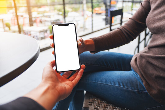 Mockup image of a woman holding and showing white mobile phone with blank black desktop screen to her friend