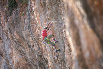 A strong man climbs a beautiful orange rock.