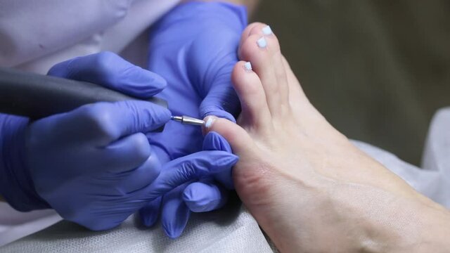 The nail technician removes the gel coat from the toenails. Hardware pedicure in the salon.