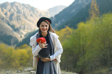 Beautiful young mother with her infant baby in sling outdoor. Woman is carrying her child and...