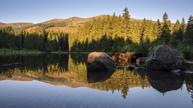 4K Time Lapse of Beautiful landscape with mountains illuminated, reflection in mountain lake, blue sky and yellow sunlight. Slovakia, Vrbicke Pleso Low Tatras