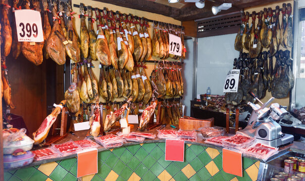 Assortment of traditional delicious Spanish meat shop with dangling legs jamon and packings of sliced ham