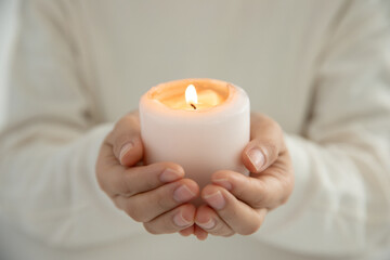 Closeup shot of hands holding an illuminated white candle