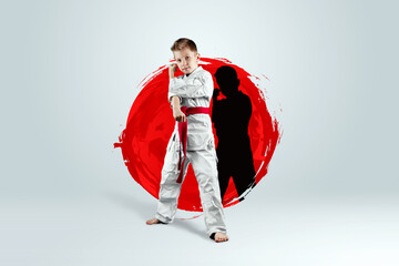Full-length portrait of a boy in a white kimono with a red belt against the background of a red...