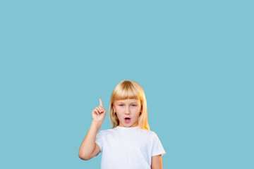 Solution idea. Advertising background. Aha moment. Knowledge discovery. Portrait of inspired surprised blonde little girl pointing up at invisible product information isolated on blue empty space.
