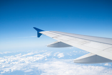 Aircraft Wing on beautiful blue sky and cloud background in altitude during flight. Wing of an airplane looking from the window.