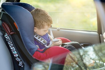 Little boy buckled up with seatbelt inside the car. Vehicle and transportation concept.