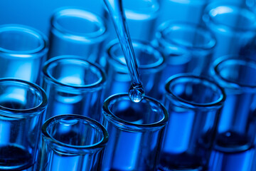 Closeup shot of a pipette tip with a droplet over glass test tubes
