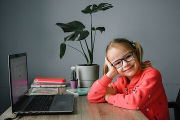 Smiling little girl in eyelgasses studying online and using her laptop at home