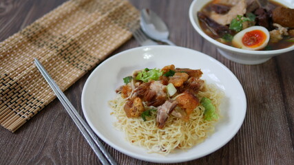 Set of Chinese noodle, a bowl of paste of rice flour over with pork egg and a plate of egg noodle with crispy pork