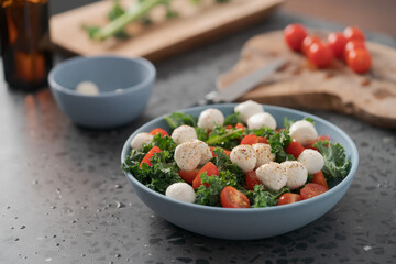 Blue bowl of salad with mozzarella, cherry tomatoes and kale on concrete countertop