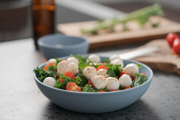 Blue bowl of salad with mozzarella, cherry tomatoes and kale on concrete countertop