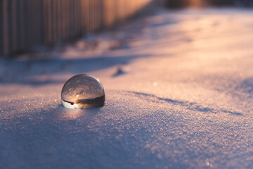glass transparent ball in the snow in winter, sun rays reflection. severe frost, cold