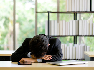 Young asian employee take a nap in the office on a table with tablet and laptop computer.