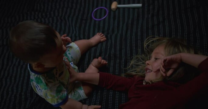 A little baby is playing with his older sibling on a bed at home