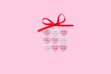 Gift box for beloved. Gift box made of tiny buttons hearts with bright red ribbon bow isolated on pink background. Present for a loved one on Valentine's day.