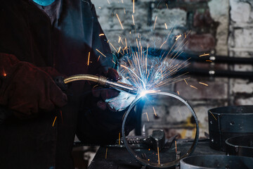Gas metal arc welding, semi-automatic welding types of ring parts, sparks and blue glow close-up.