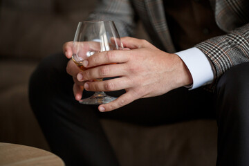A man businessman holds a glass with alcohol in his hand. Dressed in a jacket and shirt. Rest after a working day