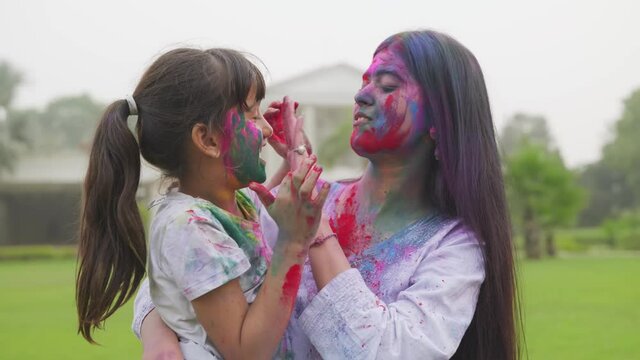 close view shot of Indian mother adoring her daughter by holding her in arms with great affection ,both of them 
 are smeared in colours and look joyful on the occasion of holi festival  