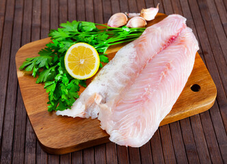 Raw fish with condiments, perch fillet with garlic, parsley and lemon on wooden table