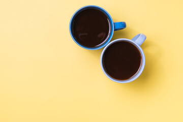 Top view of two coffee mugs on a yellow background.